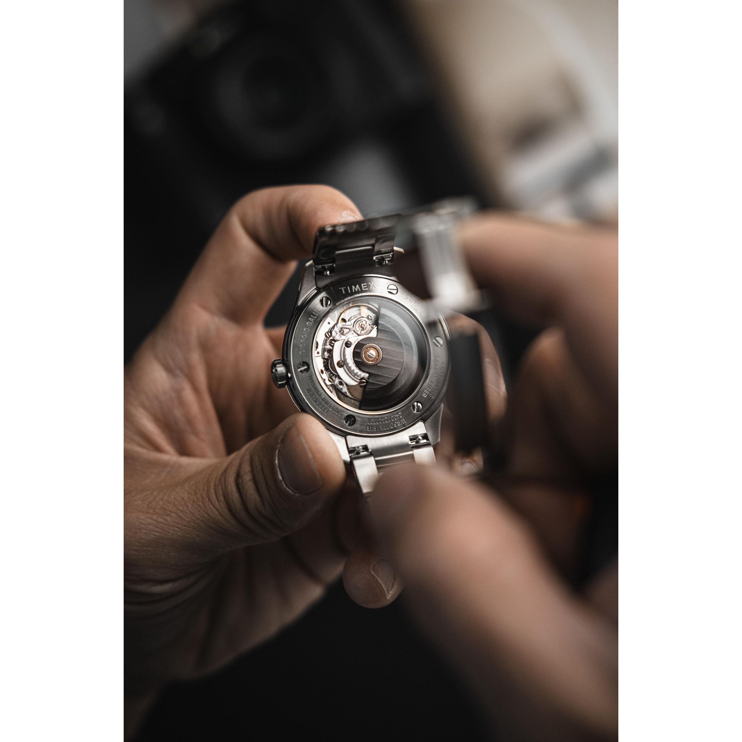 A close-up of hands holding the Timex Giorgio Galli S2Ti Automatic (38mm titanium), showcasing its exposed Swiss automatic movement and intricate gears on the back. The softly blurred background highlights the watch's craftsmanship.