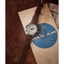 The Timex G SS QZ SW WATERBURY TRAD 41 WHITE DL 25 pilot watch, featuring a brown leather strap and stainless-steel case, sits on a vintage Pan Am envelope with part of a retro airline ticket peeking out.
