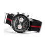 The Timex G SS QZ WTRBY HERT 39 BLK DL FABR STP 25 features a black face with two white subdials and a recycled fabric strap with a bold red stripe, shown angled to highlight side buttons and a metal buckle.