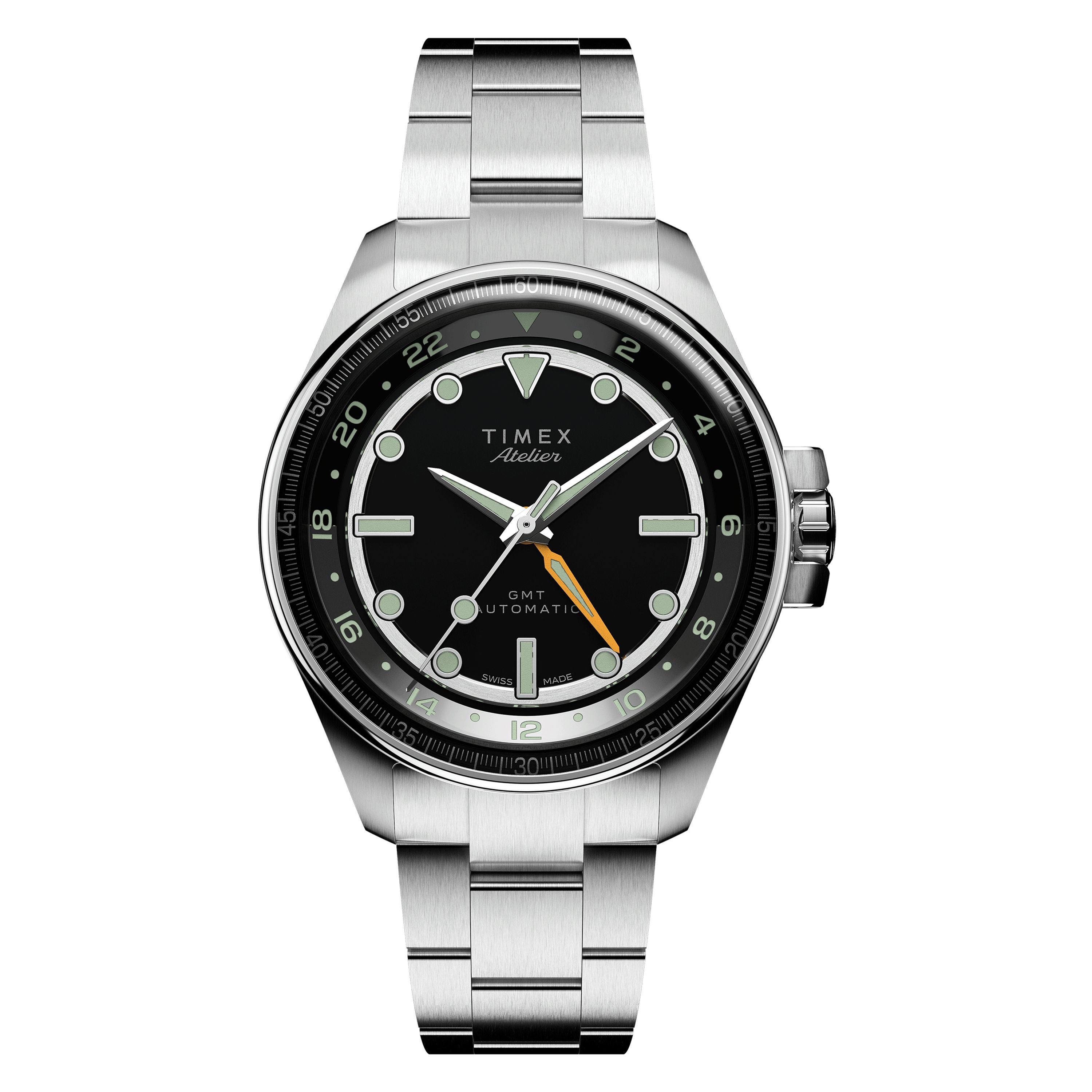 The Timex Atelier GMT24 M1a is a Swiss-made automatic watch featuring a black dial, silver markers and hands, an orange GMT hand, date window at 3 o’clock, and a sleek metal link bracelet.