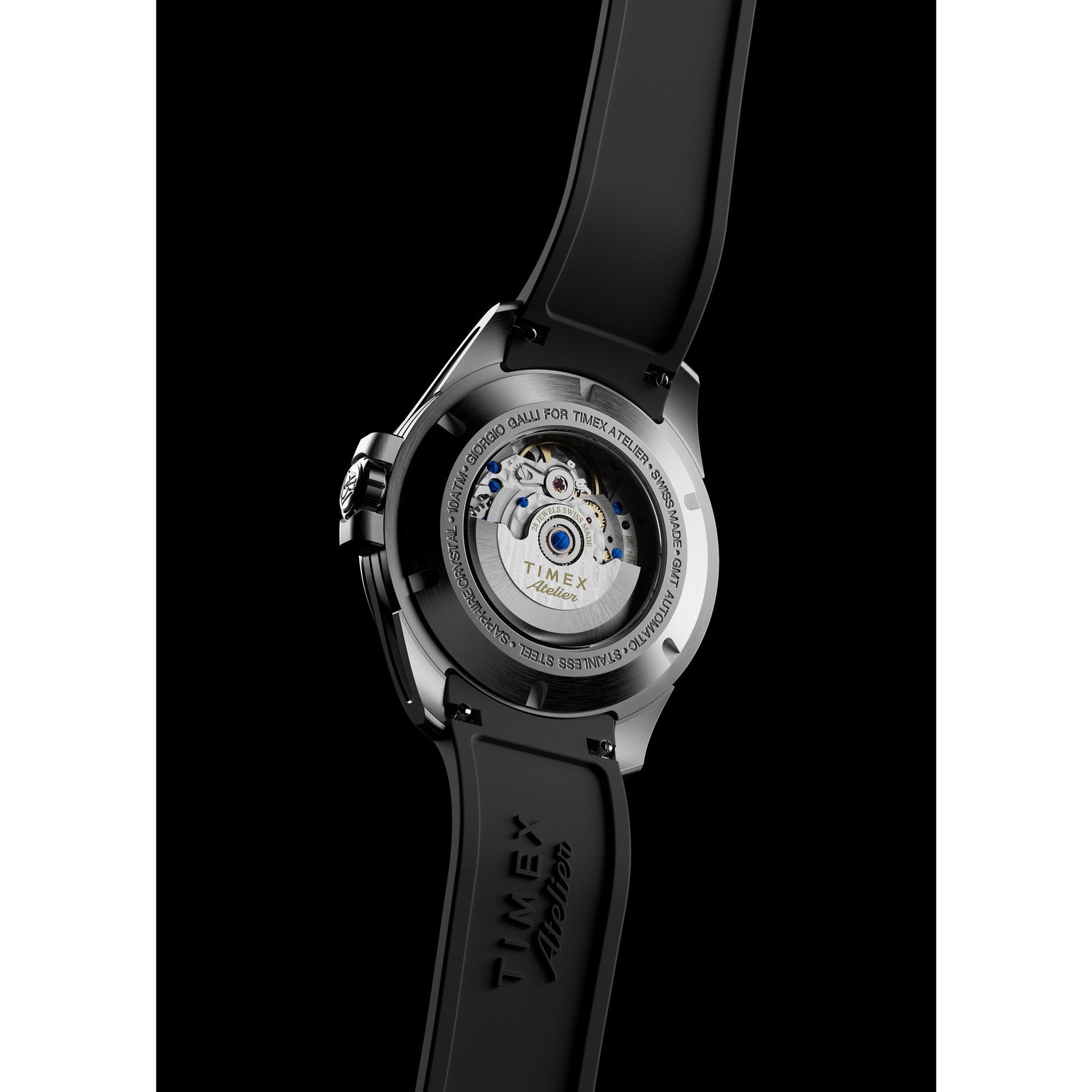 A close-up of the Timex Atelier GMT24 M1a Swiss Made Automatic watch with a black band, highlighting its exposed automatic movement through a transparent case back, set against a black background.