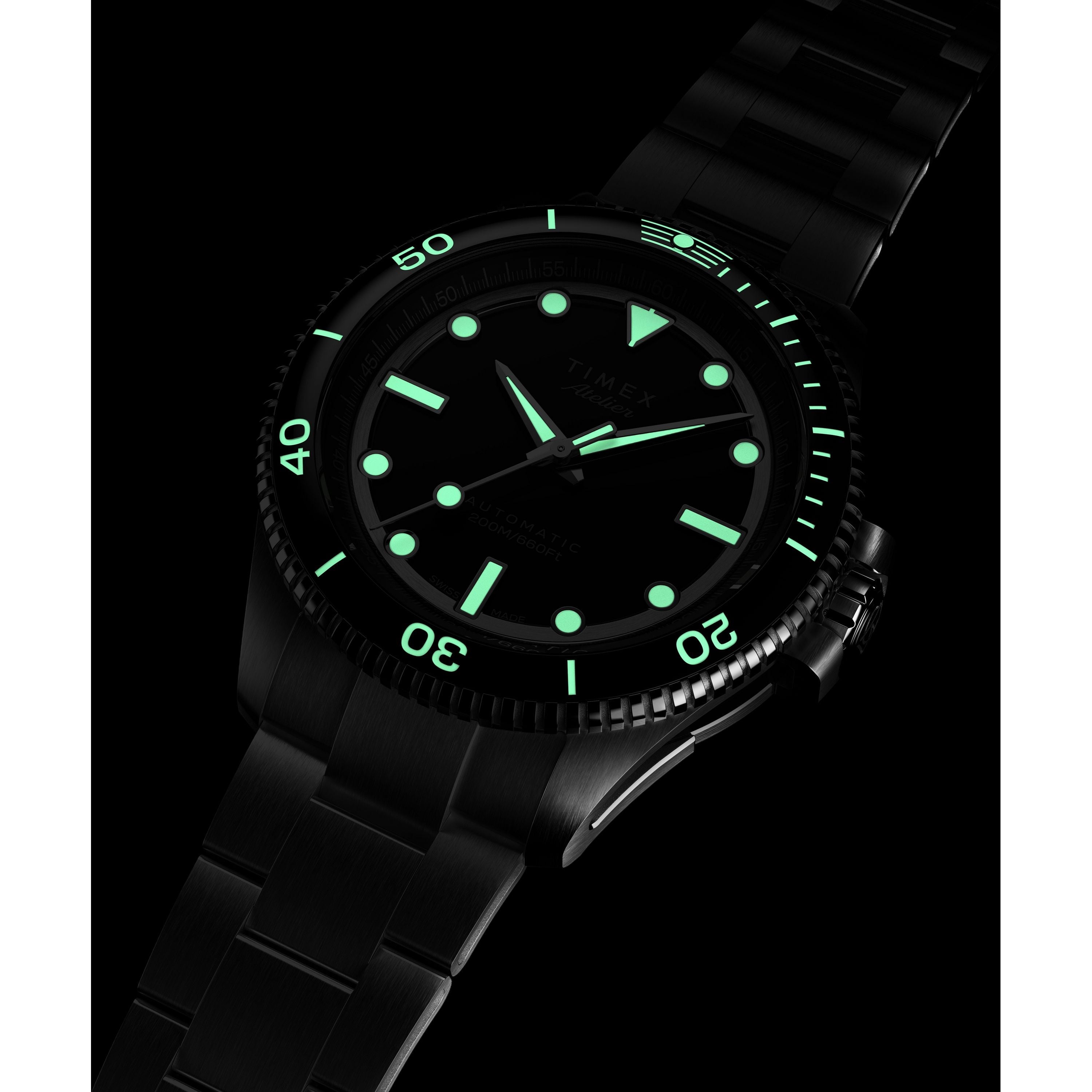 The Timex Atelier Marine M1a Swiss Made Automatic, a black metal wristwatch with luminous green hour markers and hands, glows in the dark. Its minimalist design stands out against a black background, showcasing its modern features.