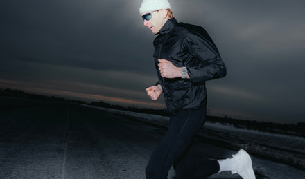 Person running at night wearing a black jacket and white beanie.