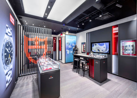 Modern watch store interior with display cases, digital screens, and branded decor in black, red, and white tones.