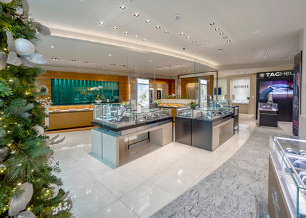Luxury jewelry store interior with glass display cases, watches, and a decorated holiday tree on the left.