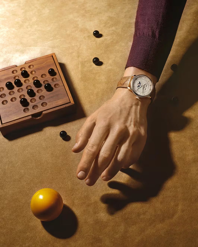 Round silver watch with cream dial and brown leather strap worn on wrist, displaying date and month complications.