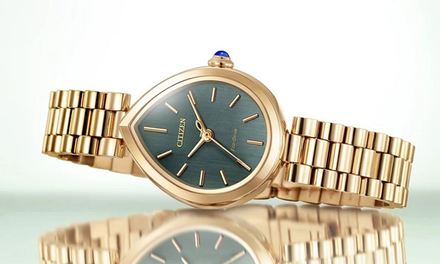 Gold wristwatch with a green face on a reflective surface