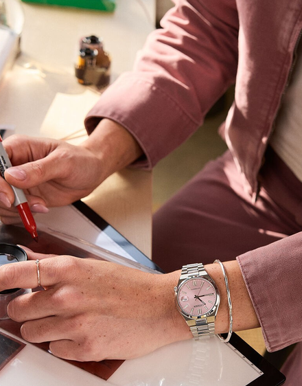 Person writing with a pen and wearing a watch, sitting at a desk.