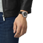 Hand wearing a watch with a black strap and silver case, against a neutral background.