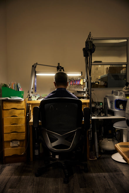 Viewed from behind, a man sits at a jeweler's bench