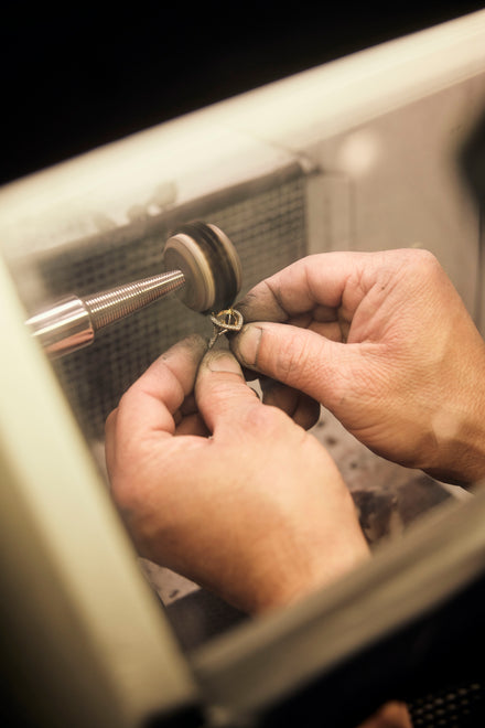 Two hands hold a ring setting against a polishing wheel