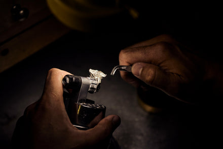 A person's hands hold a pair of tweezers and a jewelry vice with a ring on it