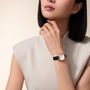 Woman wearing rectangular watch with cream dial and black leather strap on wrist.