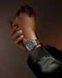 Stainless steel watch with green dial and chronograph subdials worn on wrist.