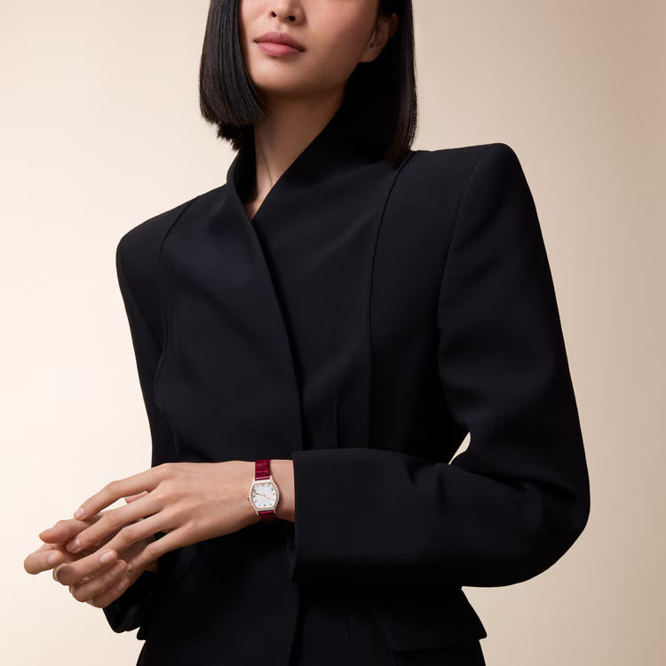 Small watch with silver case and pink leather strap worn on wrist.