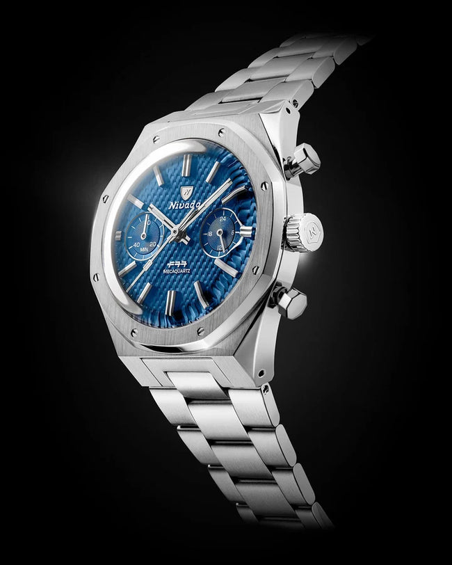 Stainless steel chronograph watch with blue dial, subdials, and link bracelet on black background.