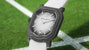 Watch with a black case and white strap on a grassy field background