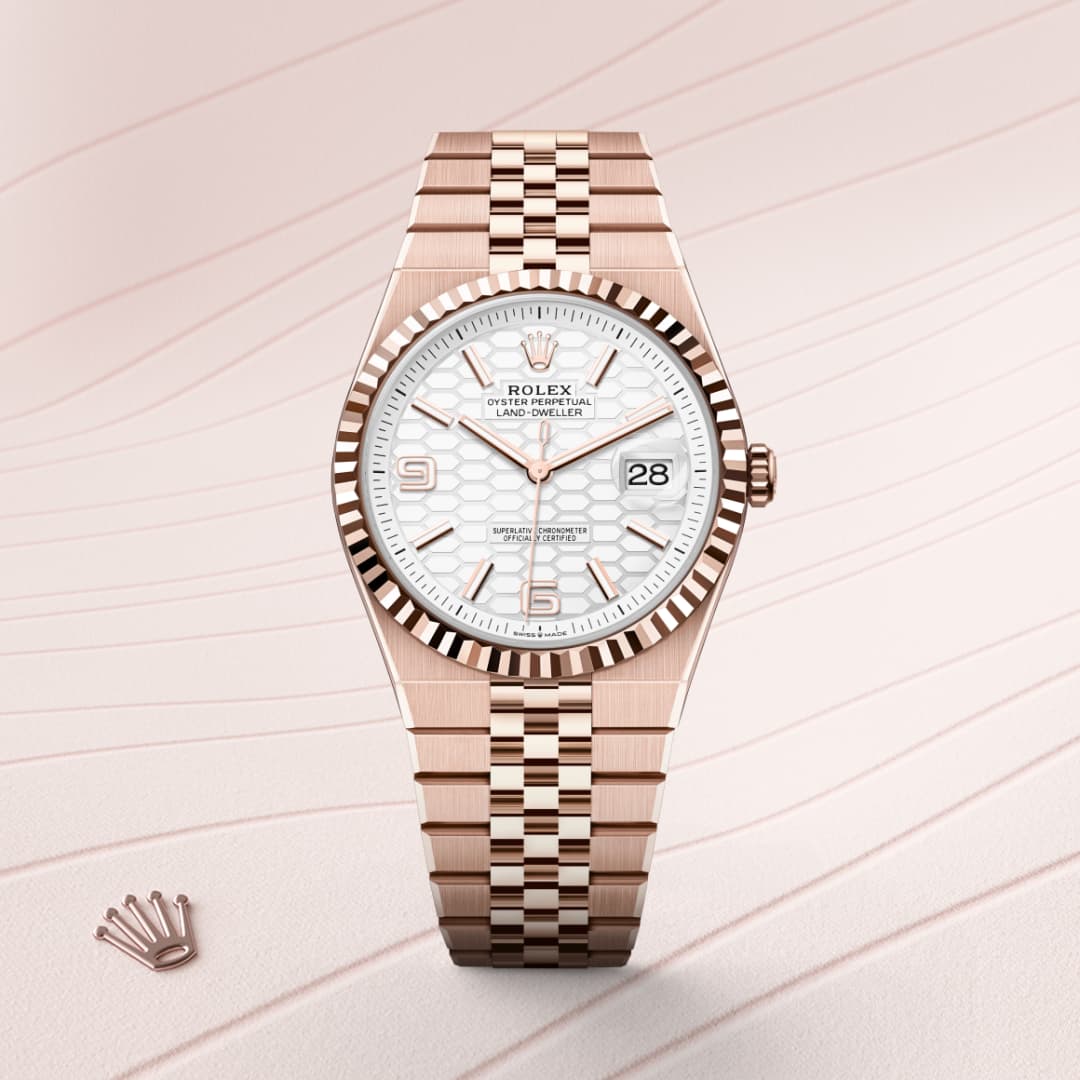 A Rolex watch with a rose gold band and white dial is displayed on a light patterned background.