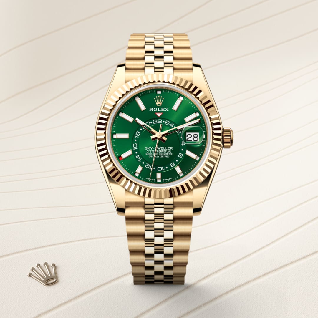 A gold Rolex Sky-Dweller watch with a green dial and date display, shown on a light textured surface.