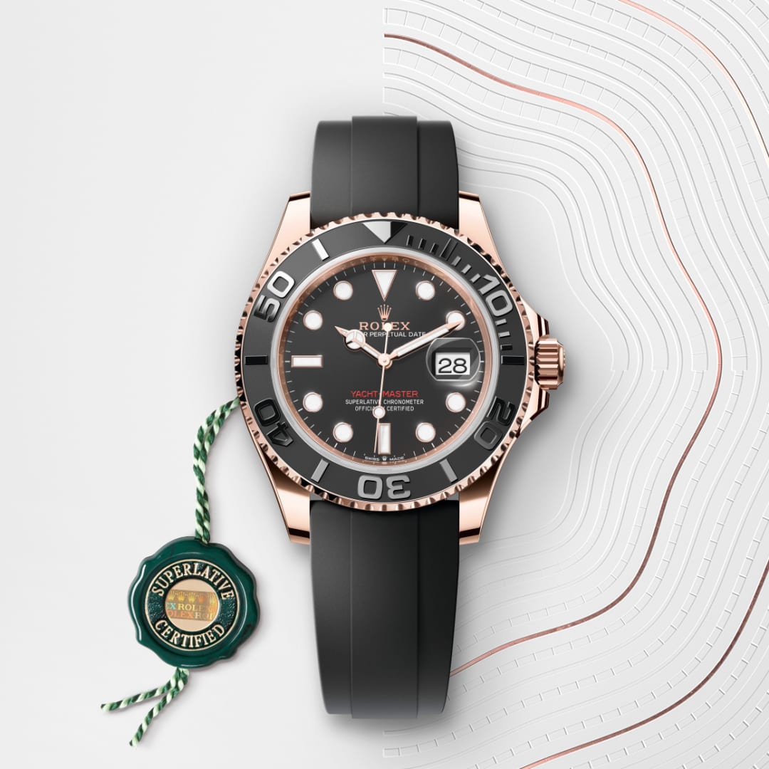 A Rolex Yacht-Master watch with a black strap and gold case, placed next to a green Superlative Certified tag.