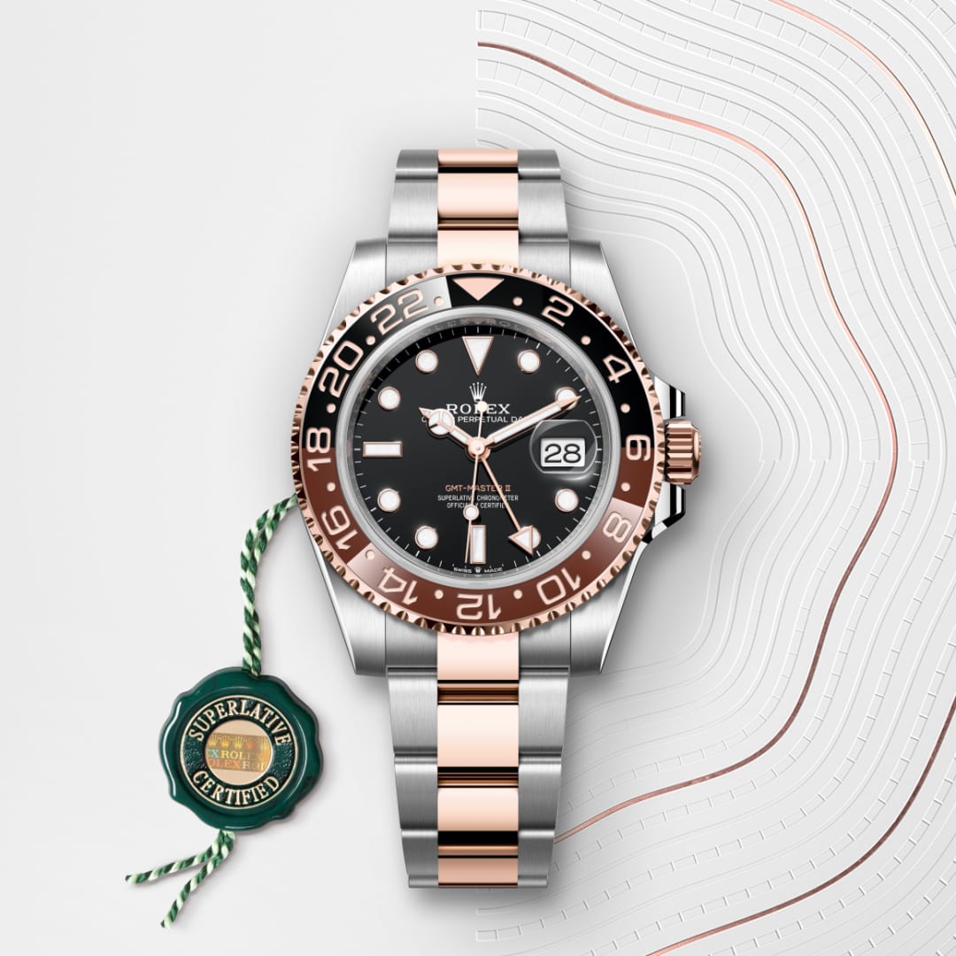 A Rolex watch with a black bezel and two-tone metal strap, next to a green Superlative Certified tag.