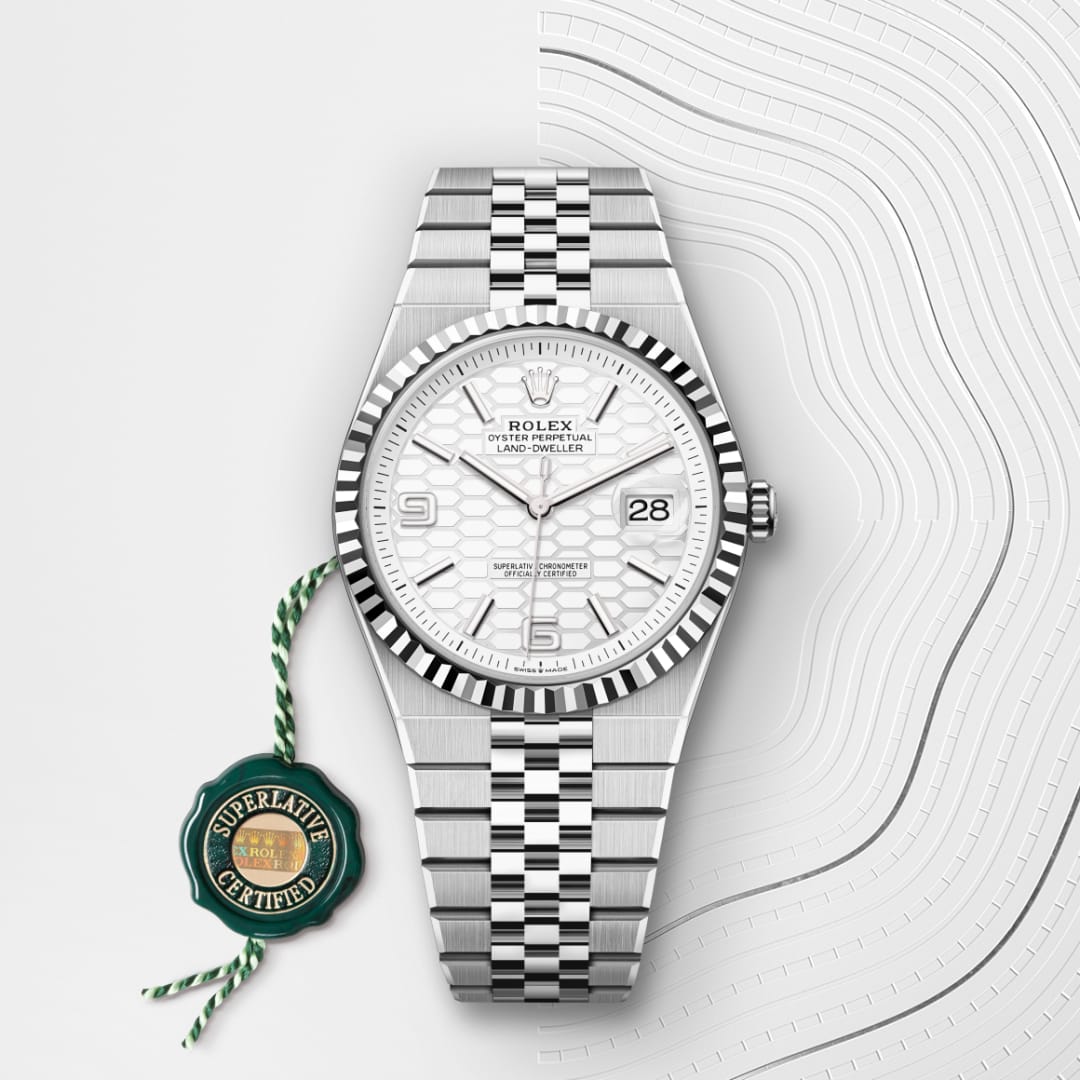 A silver Rolex watch with a white dial and date display beside a green Superlative Certified tag.