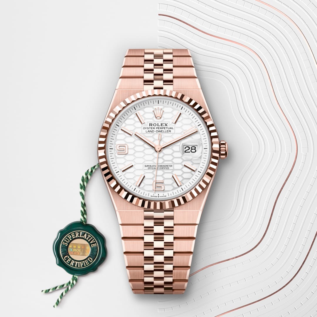 A rose gold Rolex watch with a white dial and date display, next to a green “Superlative Certified” tag.