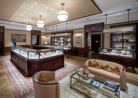 Elegant jewelry store interior with display cases, vintage rugs, and cozy seating area with beige sofas.