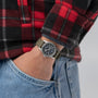 Person wearing a watch with a red and black plaid shirt and blue jeans.
