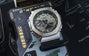 G-Shock GM2100-1ASW digital-analog watch with silver and black case on packaging background.