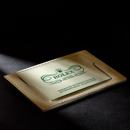 A Rolex international guarantee card in a beige leather holder, illuminated under a spotlight on a dark surface.