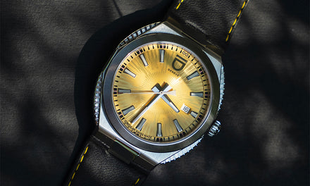 A wristwatch with a yellow dial, metal case, date display, and a black leather strap with yellow stitching.