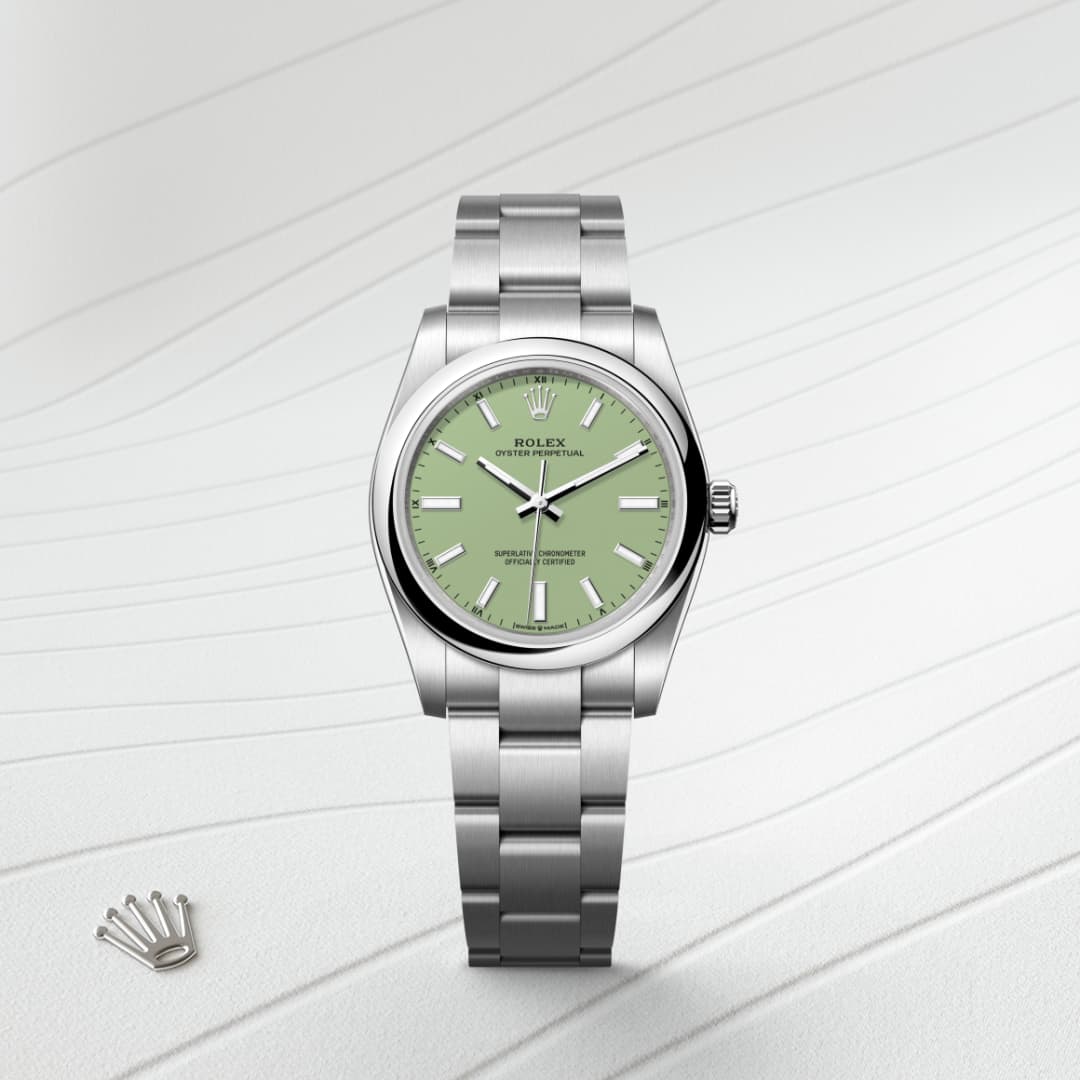 A silver Rolex watch with a green dial on a light, textured background with a small Rolex crown emblem nearby.
