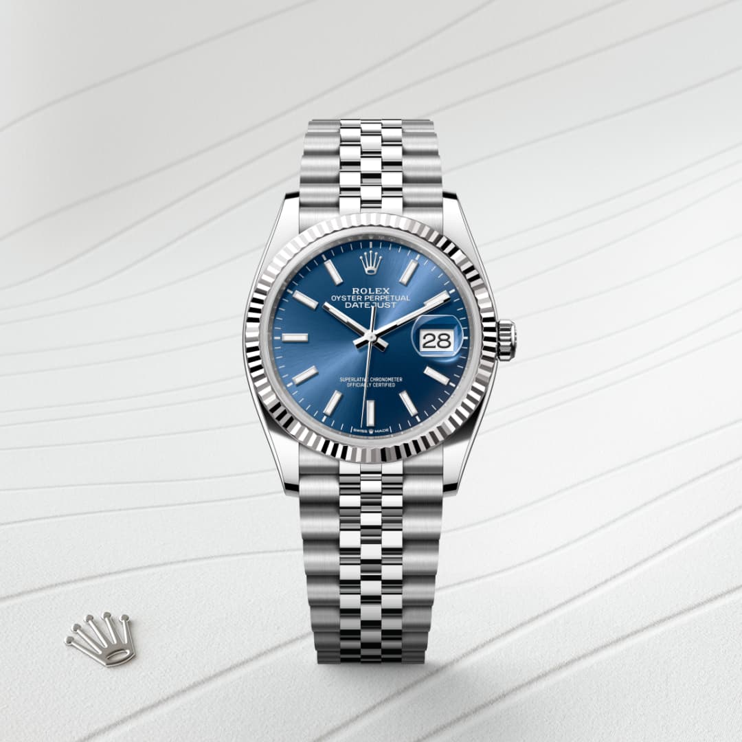 Silver Rolex watch with a blue dial and metal bracelet on a textured white surface, next to a Rolex crown logo.