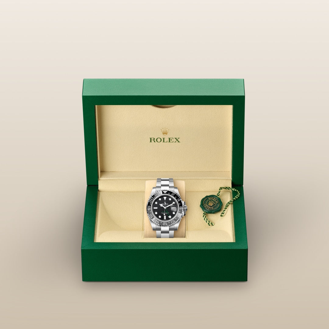 A silver Rolex watch with a black face in an open green and beige Rolex box, next to a green tag.