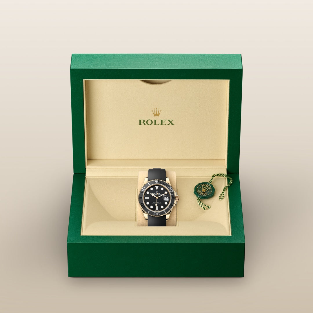 A black Rolex watch in a green and cream box with a tag, displayed on a neutral background.