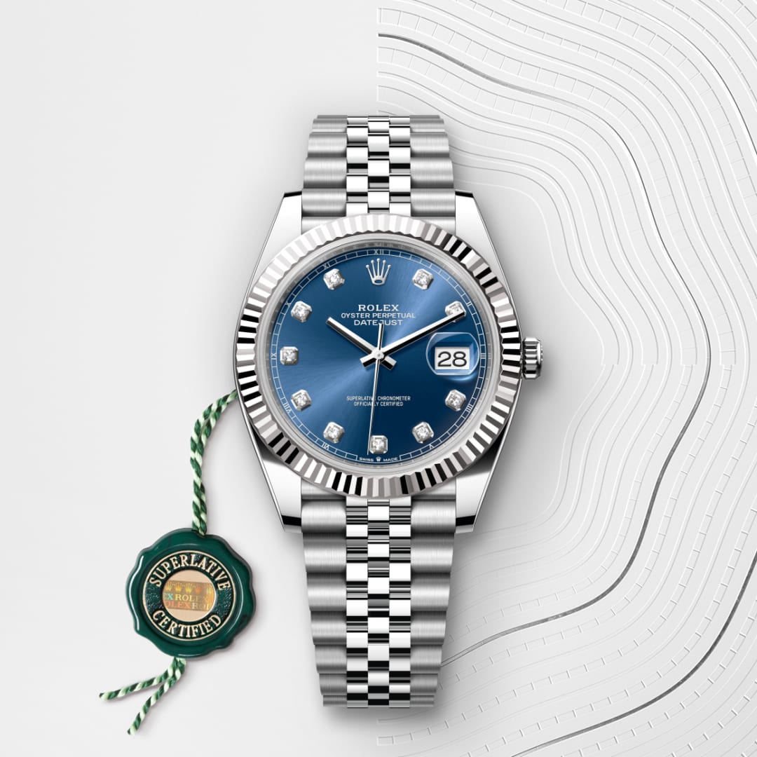 A silver Rolex watch with a blue dial and diamond hour markers, next to a green Superlative Certified tag.