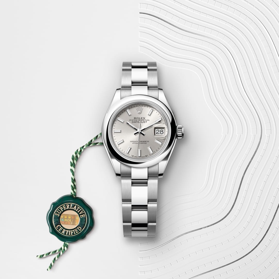 A silver Rolex watch with date display and a green Superlative Certified tag on a white, textured background.