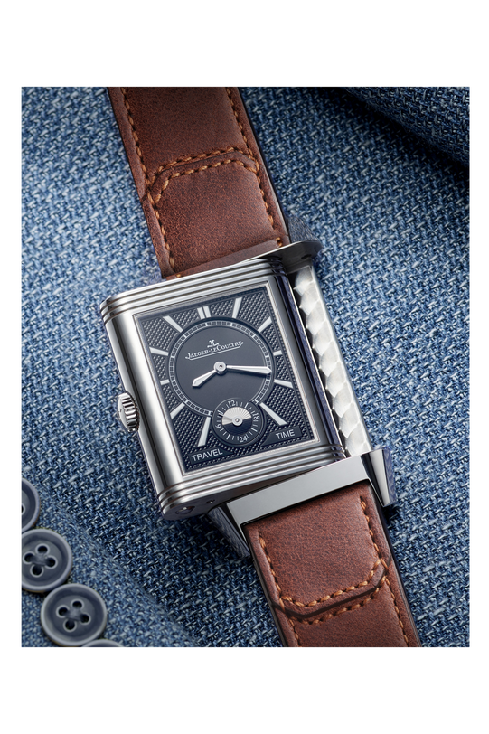 The Jaeger-LeCoultre Reverso Classic Duoface Small Seconds, a rectangular steel luxury watch with a dark patterned dial, silver details, and brown leather strap, sits on blue denim—perfect for tracking two time zones in style.