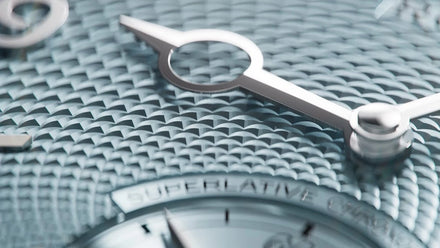 Close-up of a silver watch face with textured, patterned surface and sleek, metallic hands.
