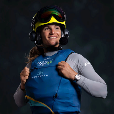 A smiling athlete in a helmet and headset wears a blue vest and gray shirt, posing confidently.