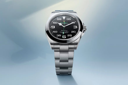 A silver Rolex Air-King watch with a black dial and stainless steel bracelet on a light blue background.