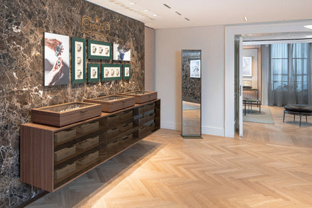 A modern jewelry showroom with display cases, framed photos, and a tall mirror against a marble accent wall.