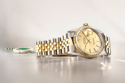 A luxury two-tone gold and silver wristwatch with a gold dial, displayed on a light surface.