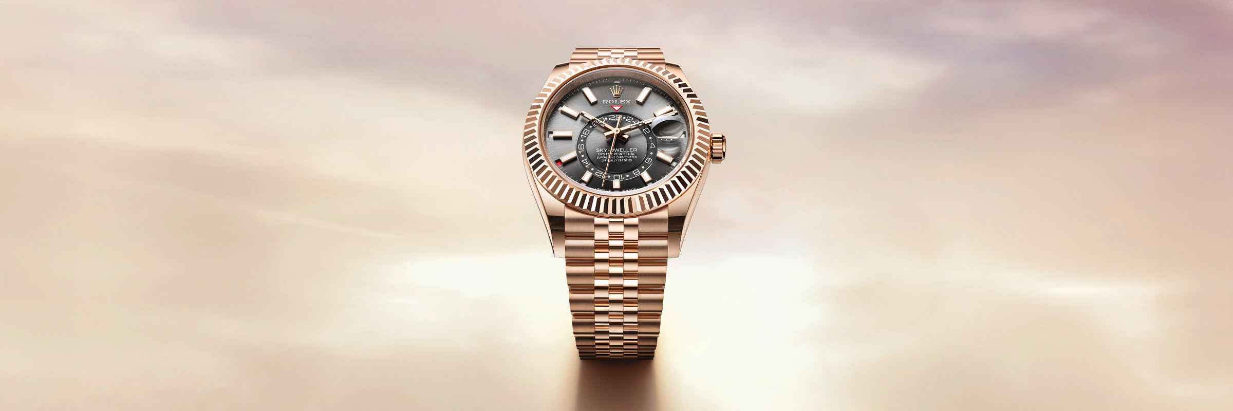 A gold wristwatch with a dark face and metal band is displayed against a soft, blurred background.