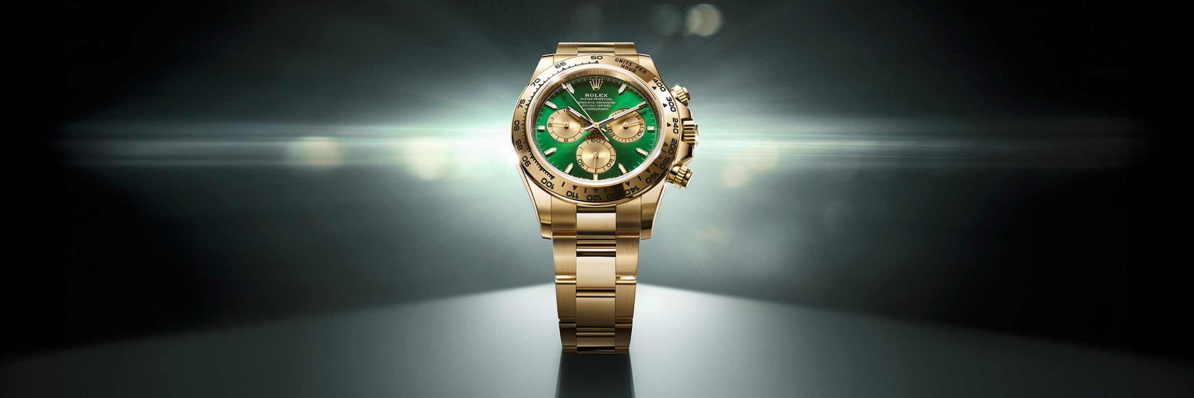 A gold wristwatch with a green face is displayed against a dark, radiant background.