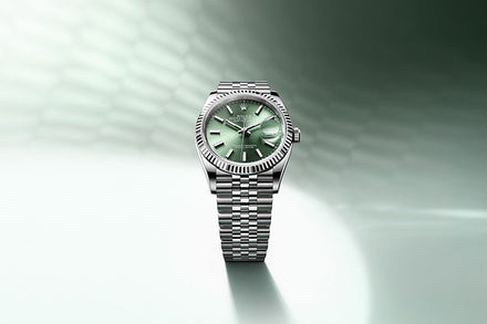 A silver Rolex Datejust wristwatch with a green dial displayed on a soft green and white gradient background.