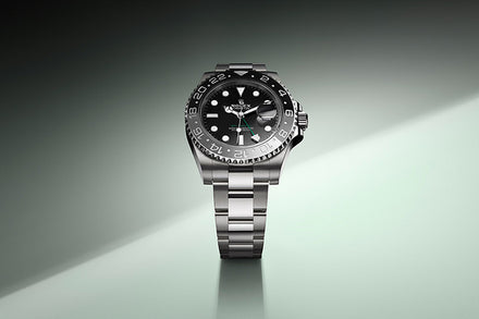 A silver Rolex GMT-Master II watch with a black dial and bezel is displayed on a gradient light background.