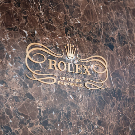 Rolex Certified Pre-Owned gold logo on a polished brown marble surface.
