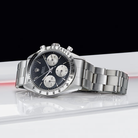 A silver luxury chronograph watch with a black dial and three subdials, displayed on a white surface.